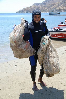 A diver emerging from the water with bags of marine pollution beach,coast,coastal,coastline,litter,pollution,human impact,plastic pollution,waste,tide,tidal,plastic,landscape,beach clean,clean,humans,people,protection,conservation,action,volunteers,volunteer